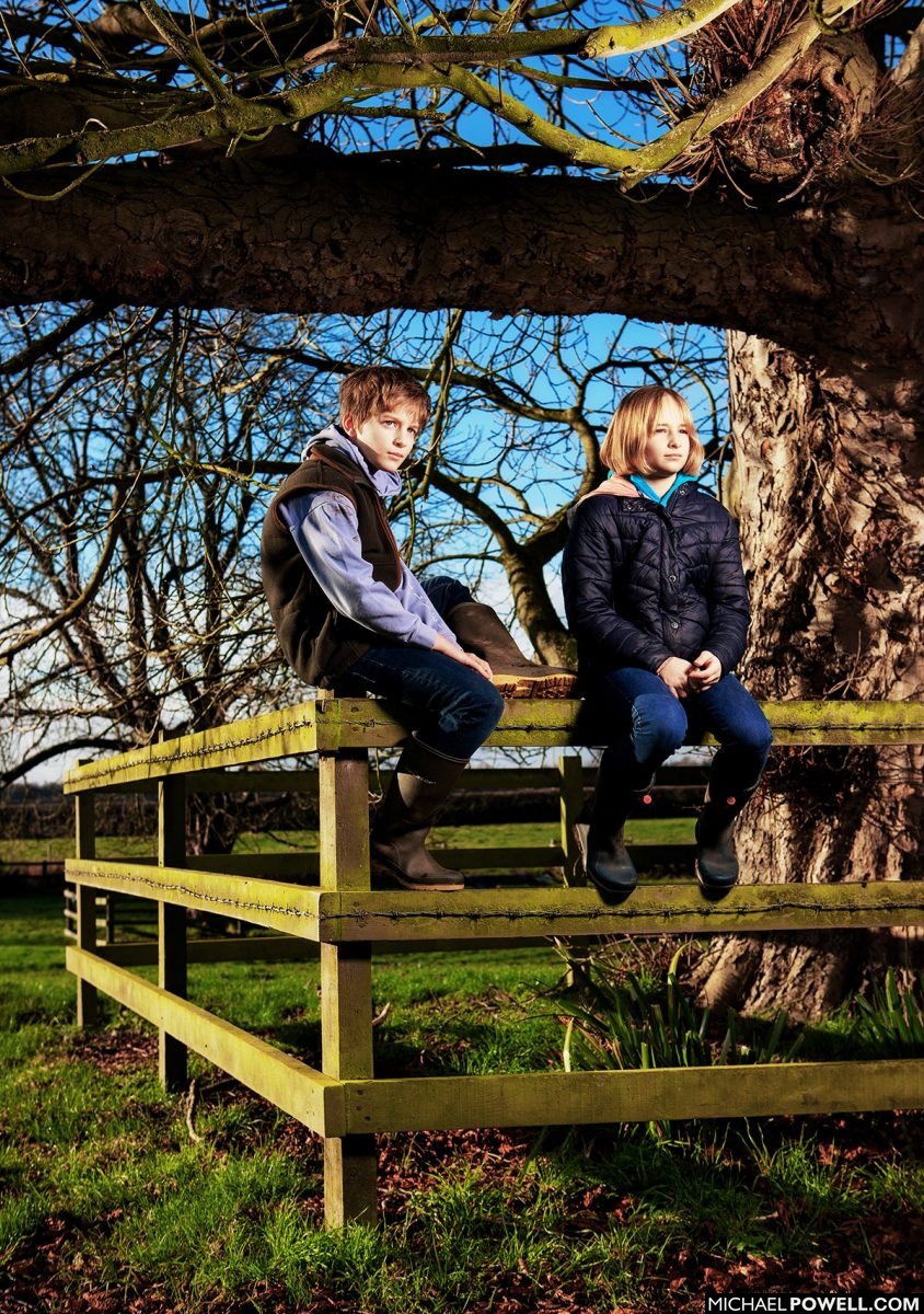 Lincolnshire family portraits of brother and sister sitting on fence in field.