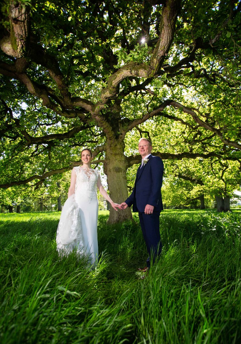 Newly married couple in Lincolnshire stand together in shade of a tree.